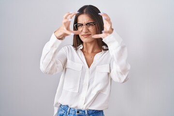 Young brunette woman wearing glasses shouting frustrated with rage, hands trying to strangle, yelling mad