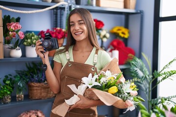 Young brunette woman working at florist shop holding camera winking looking at the camera with sexy...
