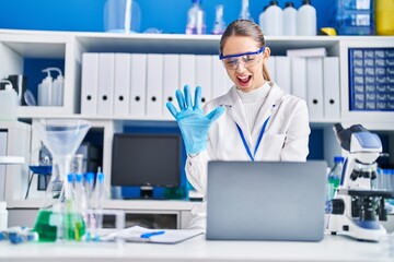 Young blonde woman working at scientist laboratory looking positive and happy standing and smiling with a confident smile showing teeth