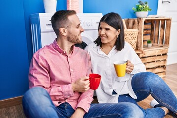Man and woman couple drinking coffee waiting for washing machine at laundry room
