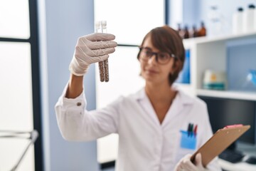 Young beautiful hispanic woman scientist holding test tubes at laboratory