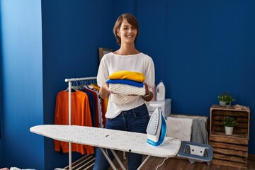 Brunette woman holding folded laundry after ironing winking looking at the camera with sexy...