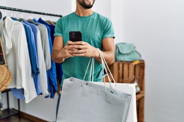 Young arab man customer using smartphone holding shopping bags at clothing store