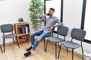 Young arab man talking on the smartphone sitting on chair at waiting room