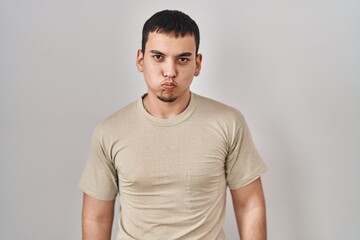 Young arab man wearing casual t shirt puffing cheeks with funny face. mouth inflated with air, crazy expression.