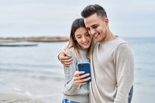 Man and woman couple hugging each other using smartphone at seaside