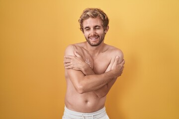 Fototapeta premium Caucasian man standing shirtless wearing sun screen hugging oneself happy and positive, smiling confident. self love and self care