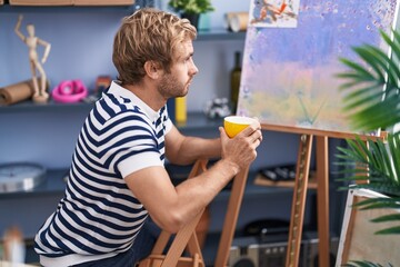 Young man artist drinking coffee sitting on chair at art studio