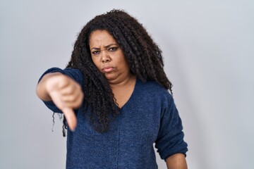 Plus size hispanic woman standing over white background looking unhappy and angry showing rejection...
