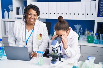 Mother and daughter scientists using microscope and laptop working at laboratory