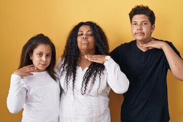 Family of mother, daughter and son standing over yellow background cutting throat with hand as knife, threaten aggression with furious violence