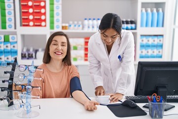 Two women pharmacist and customer measuring blood pressure at pharmacy