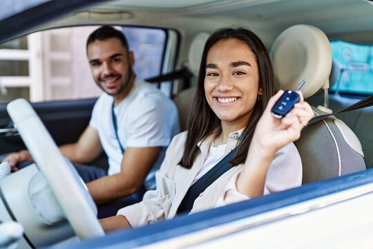 Young hispanic couple driving auto at the city. Girl smiling happy holding key of new car.
