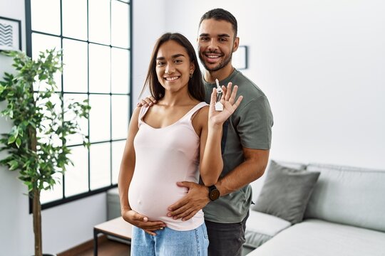 Latin man and woman couple hugging each other holding key of new house expecting baby at home