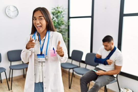 Young asian doctor woman at waiting room with a man with a broken arm pointing fingers to camera with happy and funny face. good energy and vibes.