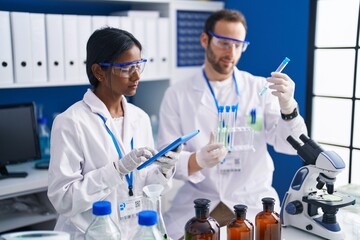 Man and woman scientists using touchpad holding test tubes at laboratory
