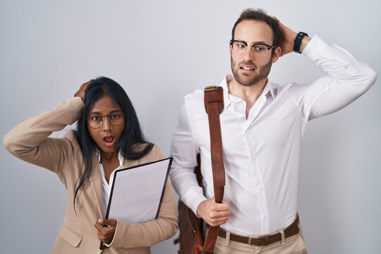Interracial business couple wearing glasses crazy and scared with hands on head, afraid and surprised of shock with open mouth