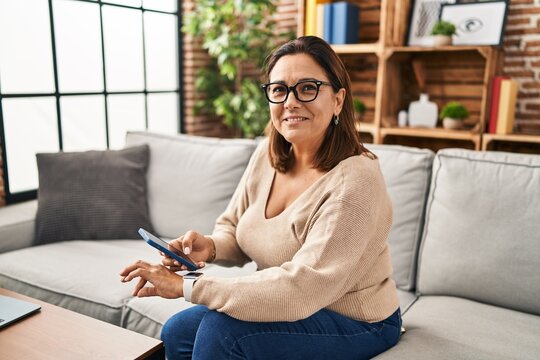 Middle age hispanic woman using smartphone and smartwatch at home