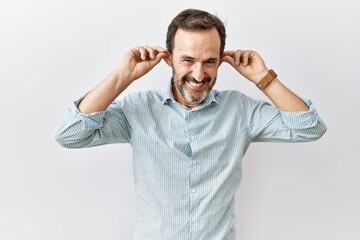 Fototapeta premium Middle age hispanic man with beard standing over isolated background smiling pulling ears with fingers, funny gesture. audition problem