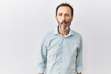 Middle age hispanic man with beard standing over isolated background making fish face with lips, crazy and comical gesture. funny expression.