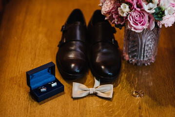 Men's accessories: wedding rings, cufflinks, bow tie and brown shoes on a wooden background. Close up. Top view.