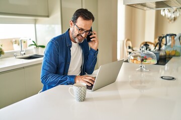 Middle age man talking on the smartphone and using laptop at home