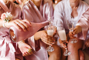 Young bridesmaids clinking with glasses of champagne in hotel room. Closeup photo of cheerful girls...