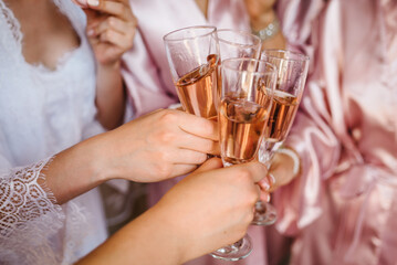 Young bridesmaids clinking with glasses of champagne in hotel room. Closeup photo of cheerful girls...