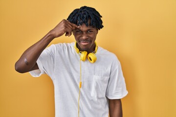 Young african man with dreadlocks standing over yellow background pointing unhappy to pimple on...