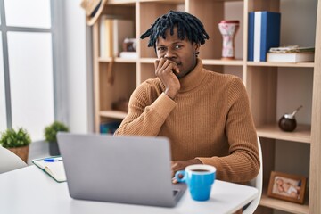 Young african man with dreadlocks working using computer laptop looking stressed and nervous with hands on mouth biting nails. anxiety problem.