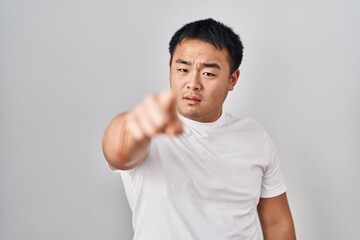 Young chinese man standing over white background pointing displeased and frustrated to the camera, angry and furious with you