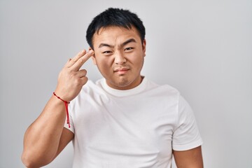 Young chinese man standing over white background shooting and killing oneself pointing hand and fingers to head like gun, suicide gesture.