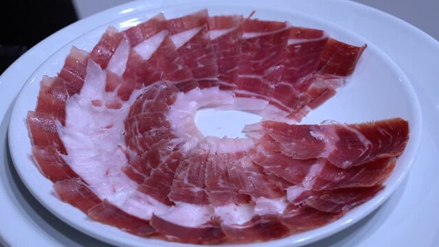 Detalle de las manos de un maestro jamonero cortando tacos de jam&oacute;n y emplat&aacute;ndolo. 