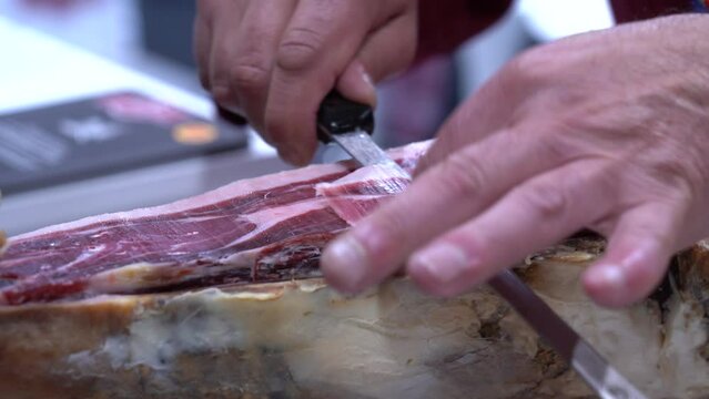 Detalle de las manos de un maestro jamonero cortando tacos de jam&oacute;n. 