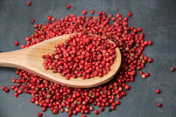 Pink pepper berries (Schinus terebinthifolia) in a wooden spoon on a black surface, top view.