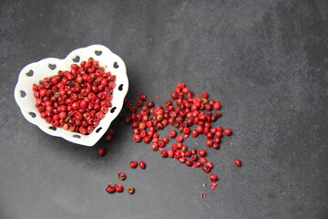 Pink pepper berries (Schinus terebinthifolia) in a heart-shaped bowl on a black surface, top view