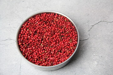 Pink pepper berries (Schinus terbinthifolia) in a metal bowl on a gray rustic background, top view.
