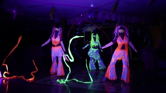 Dancers in glowing neon costumes perform in a dark room