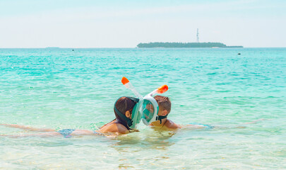 children a boy and a girl swim near the shore in a full face snorkeling mask in Maldives