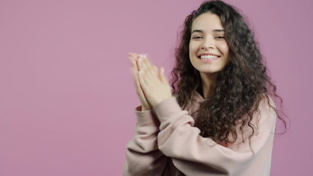 Portrait of overjoyed young woman clapping hands and smiling standing on pink background. Applause and positive emotions concept.