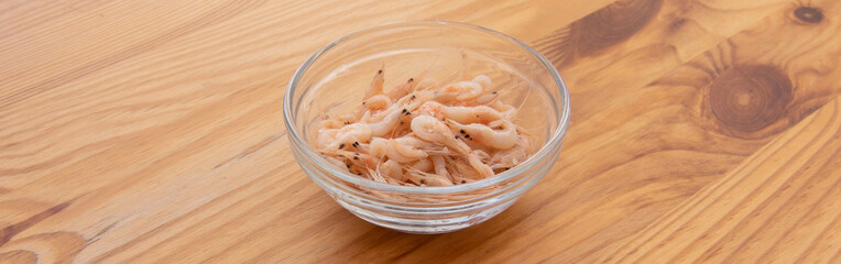Little shrimps in a glass bowl, on top of a wooden table. In Spanish called Tapa De Camarones....
