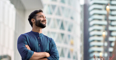 Happy wealthy rich successful indian business man standing in big city modern skyscrapers street on...