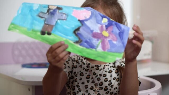 Talented Creative Child Girl Female Artist Draws Ranbow Mother summer on Paper, Child showing her work.Creates Colorful, Kid Drawing on table at Home. Painter Creating Abstract Modern Art. Childhood