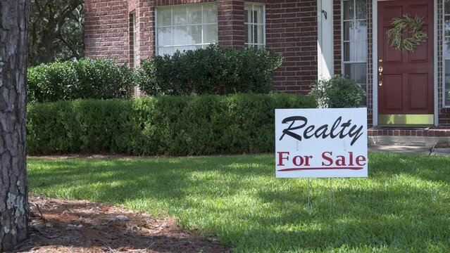 A sign in the front yard of a large brick house advertises that it is for sale.