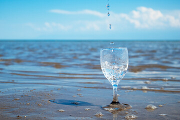 water pours into a glass against the background of the sea. clean water in a glass. water splashes