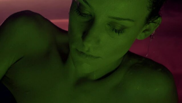 Beautiful wet girl in bikini lying in water portrait. Sidelit with neon lights..