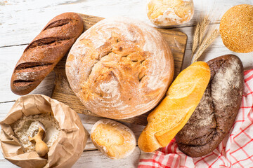 Assortment fresh bread and buns at white kitchen table. Flat lay.