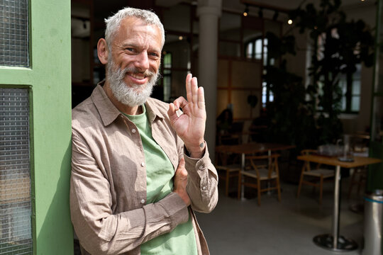 Happy older middle aged man small local business owner showing ok hand sign standing outside cafe or bar giving recommendation or feedback, suggesting good quality welcoming clients. Portrait