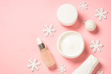 Winter cosmetic, skin care product. Cream, serum, tonic with winter decorations. Top view on pink background with copy space.