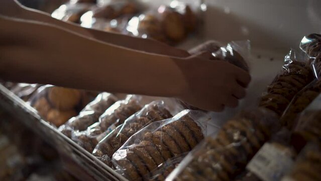 Close-up of female hands laying sweet oatmeal cookies on the counter in supermarket.